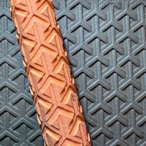 May include: Close-up of an orange foam roller with a diamond pattern. The roller is lying on a black textured surface.