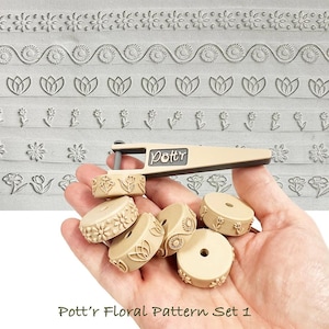 May include: A beige floral pattern set with a handle and several round stamps. The stamps feature various floral designs, including tulips, daisies, and other stylized flowers. The text "Pott'r Floral Pattern Set 1" is at the bottom.