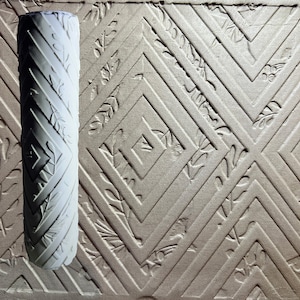 Puede incluir: Un rodillo de pintura blanco con un patrón geométrico. El rodillo está diseñado para crear un efecto texturizado en las paredes.