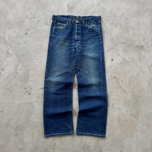 May include: A pair of blue denim jeans with a button fly and classic five-pocket design. The jeans have a faded wash and a straight leg fit. The denim is a medium weight, and the jeans appear to be pre-worn.