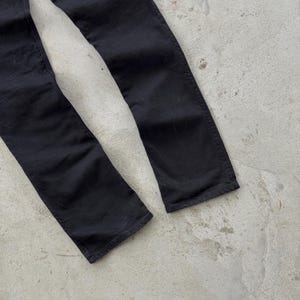 May include: Close-up of the lower portion of black denim pants. The pants are slightly faded, with visible seams and a classic straight-leg cut. The fabric appears to be a medium weight, suitable for various seasons.