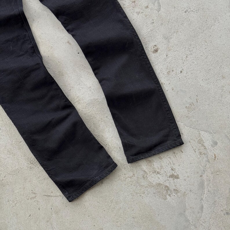 May include: Close-up of the lower portion of black denim pants. The pants are slightly faded, with visible seams and a classic straight-leg cut. The fabric appears to be a medium weight, suitable for various seasons.