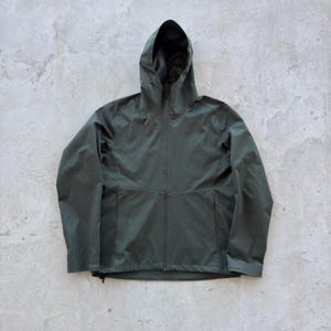 Puede incluir: Chaqueta con capucha verde oscuro con cremallera completa y dos bolsillos delanteros. La chaqueta tiene un diseño sencillo y una capucha. El material parece ser resistente al agua. Adecuada para actividades al aire libre.