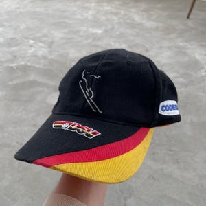 May include: A white ceramic mug with a black handle and the text "But First, Coffee" in a black, handwritten-style font. The mug is on a white surface.