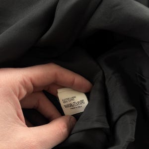 May include: A black garment interior featuring a white fabric care label. The label text reads: FUTTER/LINING 100% CUPRO, MADE IN ITALY, along with standard laundry care symbols including a crossed-out iron, crossed-out wash, and dry clean symbol.