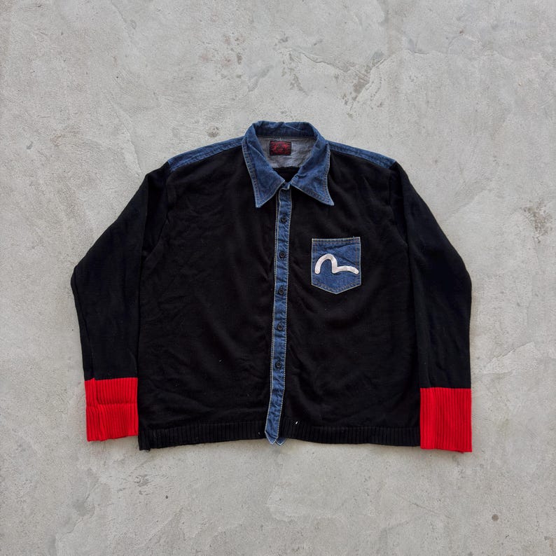 May include: Black button-up shirt with a denim collar and pocket. The shirt features red cuffs and a white logo on the denim pocket. The shirt has a denim button strip down the front.