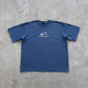 Op de afbeelding: Blauw T-shirt met korte mouwen met het Oakley-logo in wit en grijs op de voorkant. Het shirt heeft een ronde hals en is gemaakt van een zacht materiaal. Het shirt ligt plat op een grijze ondergrond.