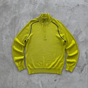 Peut inclure: Un pull chartreuse avec un col montant zippé et une bordure noire le long des épaules. Le pull à manches longues est fait d'une matière douce et est posé à plat sur une surface grise.