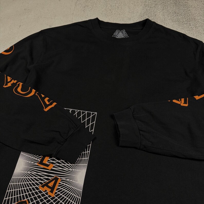 May include: Black long-sleeve t-shirt with an orange graphic print on the sleeves and a geometric design on the front. The design features a grid pattern with a radiating effect and the word "L.A." in the center.