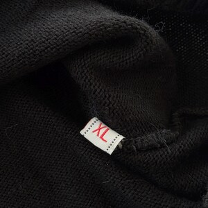 May include: Close-up of black fabric with a small rectangular tag. The tag is white with the letters "XL" in red. The fabric appears to be a knit or woven material.