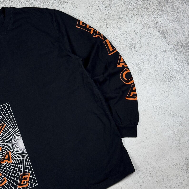 May include: Black long-sleeve shirt with an orange graphic of a geometric design and the word "Palace" on the sleeve.
