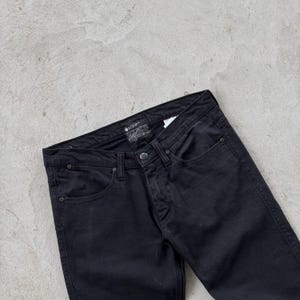 May include: Black denim jeans with a classic five-pocket design. The jeans feature a button and zipper closure, along with rivets at the pocket corners. The dark wash gives them a versatile look.