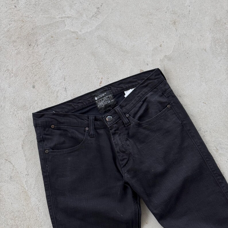 May include: Black denim jeans with a classic five-pocket design. The jeans feature a button and zipper closure, along with rivets at the pocket corners. The dark wash gives them a versatile look.