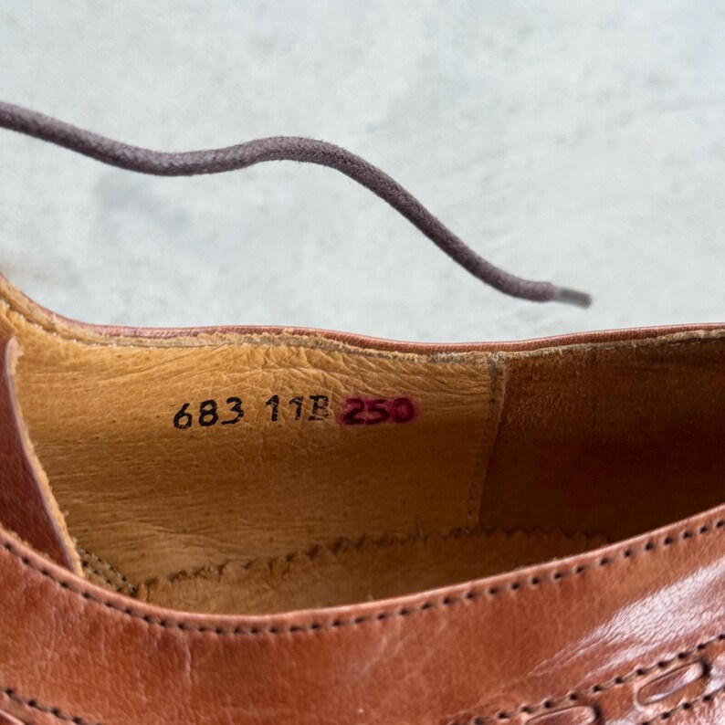 Puede incluir: Primer plano del interior de un zapato de cuero marr&oacute;n con los n&uacute;meros 683 11B 250 impresos en la plantilla.