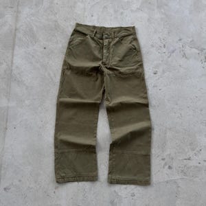 May include: Olive green utility trousers featuring a button fly closure, two front pockets, and reinforced double-layer fabric panels at the knees. These straight-leg trousers have a structured waistband with belt loops and visible topstitching.