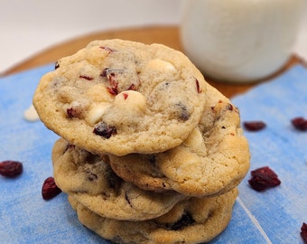 May include: A stack of four white chocolate cranberry cookies on a blue and white patterned surface. The cookies are soft and chewy, with white chocolate chips and cranberries throughout.
