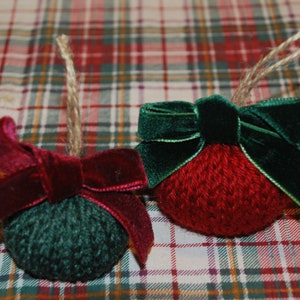 May include: Two handmade knitted Christmas ornaments with velvet bows. One ornament is red and the other is green.