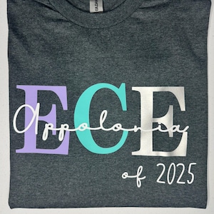 May include: Dark grey t-shirt featuring the letters "ECE" in lavender, teal, and silver. The word "Appolonia" is written in cursive over the "E" and "C". The text "of 2025" is below the letters.