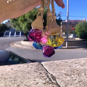 May include: Four colorful glass car air fresheners with wooden tags. The tags have the word "Perfume" written on them. The fresheners are hanging from strings.