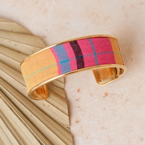 May include: A gold bangle bracelet with a pink, yellow, and blue plaid fabric covering. The fabric has a subtle sheen.