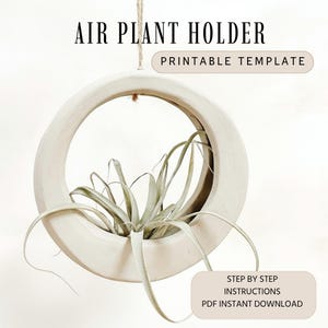 May include: A cream-colored air plant holder with a circular design, suspended by a natural fiber cord. The holder contains a green air plant. Text on the image reads "AIR PLANT HOLDER" and "PRINTABLE TEMPLATE". Additional text states "STEP BY STEP INSTRUCTIONS PDF INSTANT DOWNLOAD".