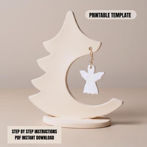 May include: A cream-colored earring display stand in a tree and crescent moon shape, holding a white angel-shaped earring. The stand has the text "PRINTABLE TEMPLATE" and "STEP BY STEP INSTRUCTIONS PDF INSTANT DOWNLOAD".