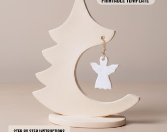Puede incluir: Un expositor de pendientes de color crema con forma de árbol y media luna, que sostiene un pendiente blanco en forma de ángel. El expositor tiene el texto "PRINTABLE TEMPLATE" y "STEP BY STEP INSTRUCTIONS PDF INSTANT DOWNLOAD".