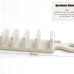 May include: A cream-coloured ceramic utensil holder with four vertical dividers and a handle. The holder is approximately 11 cm tall, 6 cm wide, and 30 cm long. The text "Aproximate Dimensions" is visible.