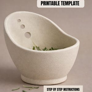 a white ceramic bowl with a few holes in it, placed on a surface with some green leaves scattered around it.