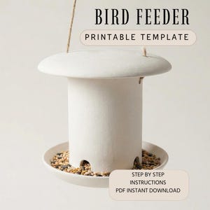 May include: A cream-coloured bird feeder with a circular top and a cylindrical body, filled with birdseed. The feeder is suspended by a natural fibre rope. Text on the image reads "BIRD FEEDER PRINTABLE TEMPLATE" and "STEP BY STEP INSTRUCTIONS PDF INSTANT DOWNLOAD."