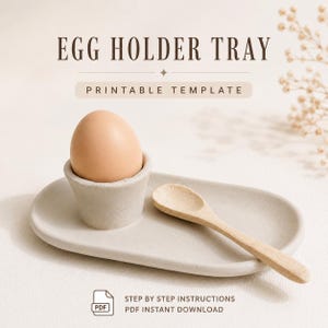 Puede incluir: Una bandeja ovalada de color gris claro para huevos con una copa integrada que sostiene un huevo marrón. Una pequeña cuchara de madera descansa sobre la bandeja. El texto dice EGG HOLDER TRAY PRINTABLE TEMPLATE y STEP BY STEP INSTRUCTIONS PDF INSTANT DOWNLOAD.