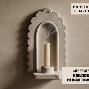 a white candle holder with a lit candle inside, set against a plain beige wall.
