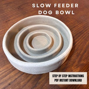 Puede incluir: Un comedero lento para perros de cerámica gris con un diseño en espiral. El cuenco tiene una superficie texturizada. El texto "SLOW FEEDER DOG BOWL" está en la parte superior. El texto "STEP BY STEP INSTRUCTIONS PDF INSTANT DOWNLOAD" está en la parte inferior.