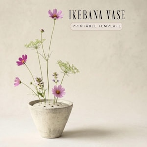 Op de afbeelding: Een betongrijze Ikebana vaas met roze cosmosbloemen en fijne groene takjes. De vaas heeft een brede opening met meerdere gaten om stelen te rangschikken. De tekst "IKEBANA VASE PRINTABLE TEMPLATE" staat boven de vaas.