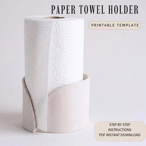 Puede incluir: Un rollo de papel de cocina blanco se encuentra en un soporte de cerámica beige claro. El soporte tiene un diseño curvo. El texto en la parte superior dice "PAPER TOWEL HOLDER". El texto adicional dice "PRINTABLE TEMPLATE" y "STEP BY STEP INSTRUCTIONS PDF INSTANT DOWNLOAD".