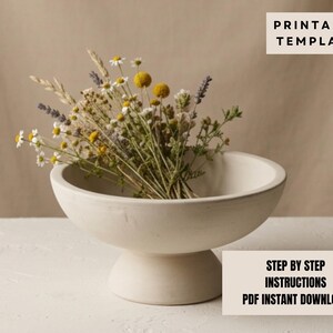 a white ceramic bowl filled with a bouquet of dried flowers, placed on a white surface.