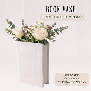 May include: A white book-shaped vase filled with white roses, daisies, and greenery. The text "BOOK VASE PRINTABLE TEMPLATE" is at the top. Below the vase, the text reads "STEP BY STEP INSTRUCTIONS PDF INSTANT DOWNLOAD."
