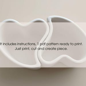 May include: Two white heart-shaped objects are connected, with the text "It includes instructions, 1 pdf pattern ready to print. Just print, cut and create piece." The objects are on a light background.
