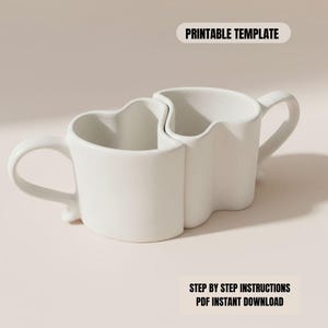May include: Two white ceramic mugs designed to fit together, forming a heart shape. Each mug has a handle and a unique wavy top edge. The text "PRINTABLE TEMPLATE" and "STEP BY STEP INSTRUCTIONS PDF INSTANT DOWNLOAD" are visible.