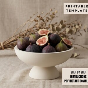 a white bowl filled with sliced figs, placed on a beige cloth. The bowl is positioned on a table, with a bunch of dried branches or twigs nearby. The image also includes a "PRINTABLE TEMPLATE" label and a "STEP BY STEP INSTRUCTIONS" label, suggesting that the image is a template for creating a similar arrangement.