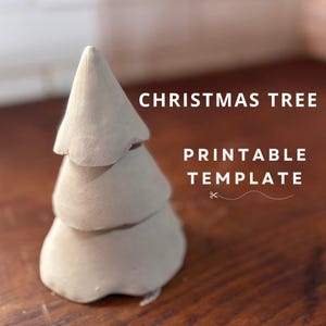 以下が含まれることがあります： 白い3段の粘土製のクリスマスツリーのオーナメント。オーナメントは木製の表面の上に置かれています。オーナメントの上に「CHRISTMAS TREE PRINTABLE TEMPLATE」というテキストがあります。