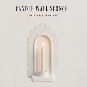 May include: A white ceramic candle wall sconce with a scalloped edge design. The sconce features an arched opening holding a lit, off-white candle. The text "CANDLE WALL SCONCE" and "PRINTABLE TEMPLATE" are at the top.