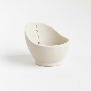 A simple, white ceramic bowl with three holes on the side.