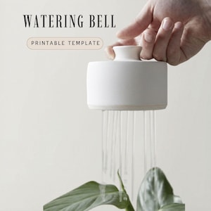 Könnte beinhalten: Eine weiße Keramik-Gießglocke mit dem Text "WATERING BELL" und "PRINTABLE TEMPLATE". Die Glocke bewässert eine grüne Pflanze. Die Glocke wird von einer Hand gehalten.