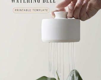 Pode incluir: Um sino de rega de cerâmica branca com o texto "WATERING BELL" e "PRINTABLE TEMPLATE". O sino está a regar uma planta verde. O sino está a ser segurado por uma mão.