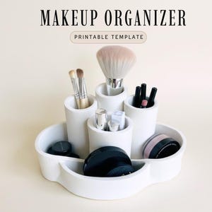 Puede incluir: Un organizador de maquillaje blanco con múltiples compartimentos y soportes cilíndricos. El organizador contiene varios artículos de maquillaje, incluyendo brochas, pintalabios y polvos compactos. El texto "MAKEUP ORGANIZER" y "PRINTABLE TEMPLATE" se muestra en la parte superior.