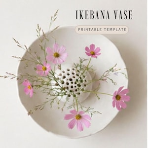 May include: A white ceramic Ikebana vase with a perforated floral holder, holding pink cosmos flowers and green foliage. The text "IKEBANA VASE" and "PRINTABLE TEMPLATE" are displayed above the vase.