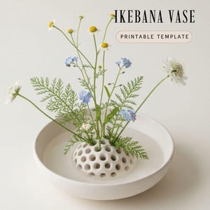 Może przedstawiać: Biały ceramiczny wazon Ikebana z perforowanym uchwytem na kwiaty, wypełniony wodą i świeżymi kwiatami. Kompozycja zawiera stokrotki, niebieskie niezapominajki i zielone liście. Wyświetlany jest tekst "IKEBANA VASE" i "PRINTABLE TEMPLATE".