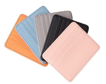 May include: Five leather card holders in different colors: orange, light blue, gray, black, and pink. Each holder has multiple card slots.