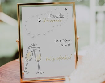 May include: A gold-framed sign with the words "Pearls & Prosecco" and "Custom Sign" in black and gold lettering. The sign features a pearl necklace design and illustrations of champagne flutes. The text "fully editable!" is also included.